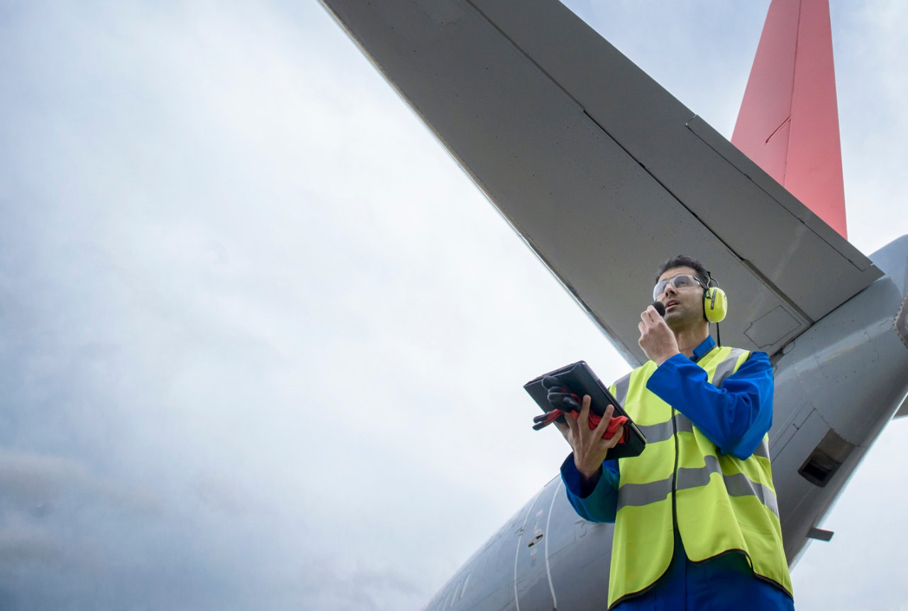 Airside engineer talking on radio near aircraft on runway