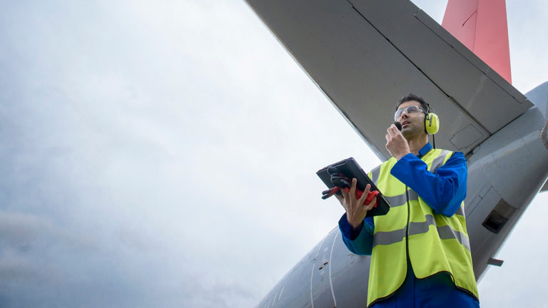 Airside engineer talking on radio near aircraft on runway