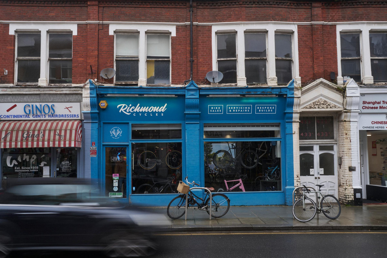 blue bicycle shop on a rainy street with parked bikes and passing car