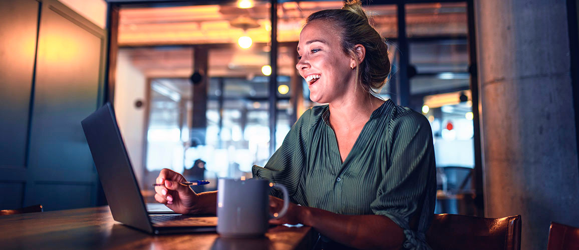 smiling lady working in coffee shop looking at laptop screen