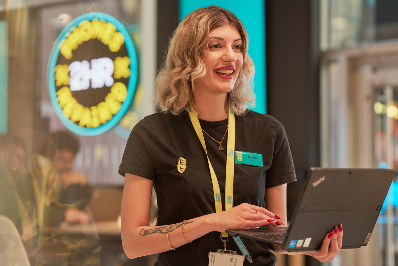 EE guide Sophie holding a laptop in an EE store