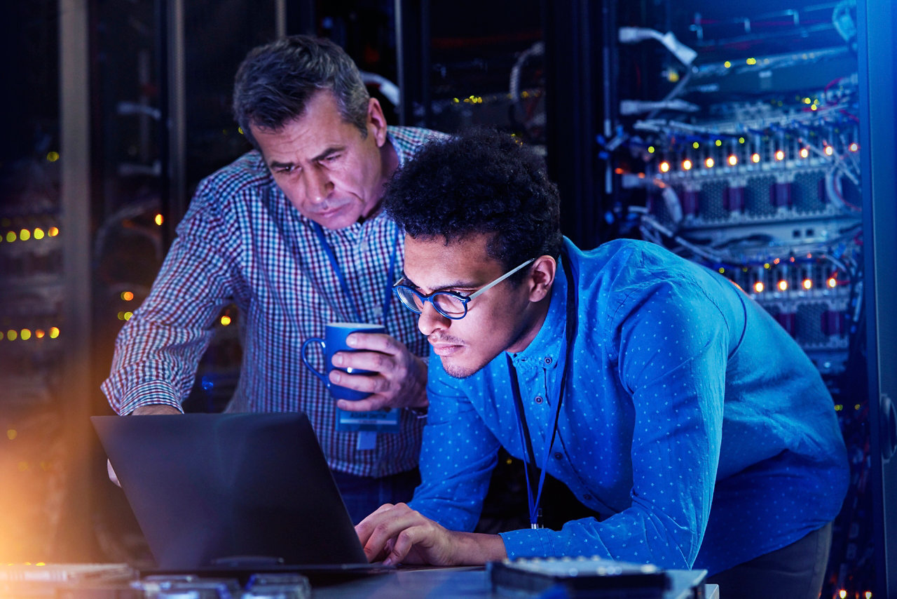 Engineers in server room look at laptop