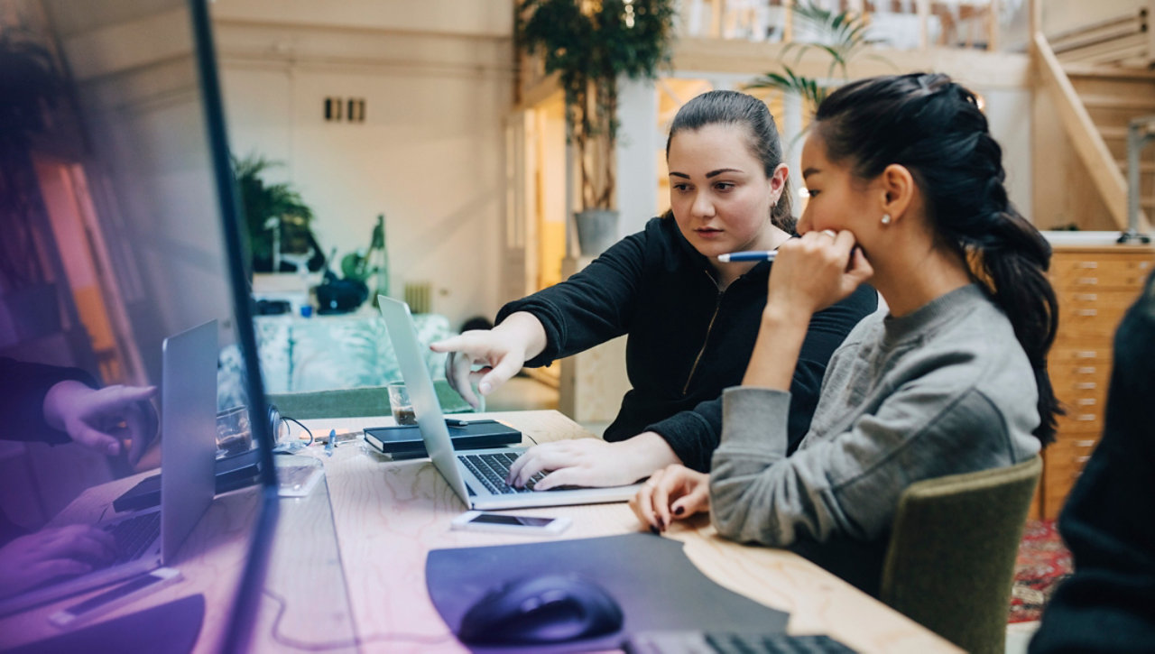 female coworkers discussing coding on laptop while sitting in office