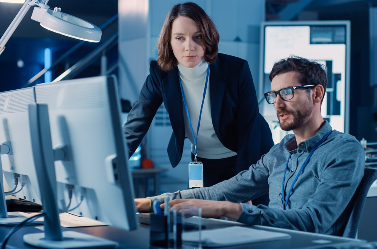 seated man and standing woman looking at screen