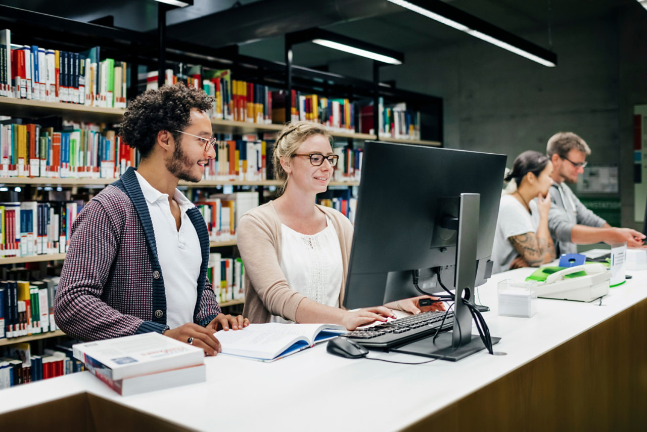 Group of students using library computer to find books