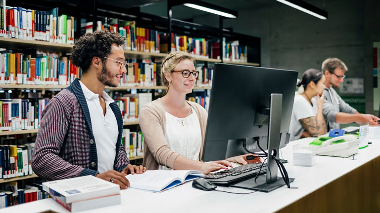 Group of students using library computer to find books