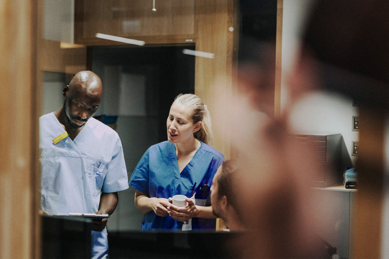two healthcare workers in scrubs discussing something on a clipboard