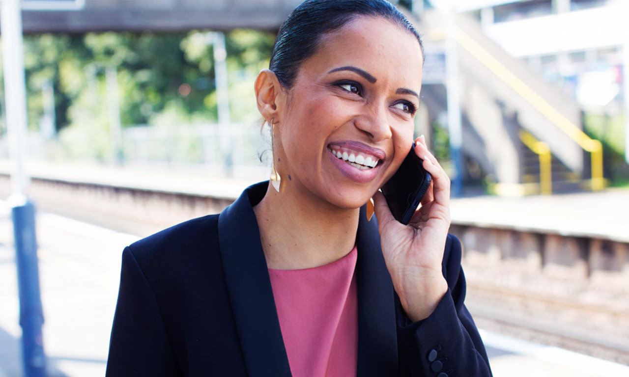 lady on station platform smiling listening on mobile phone