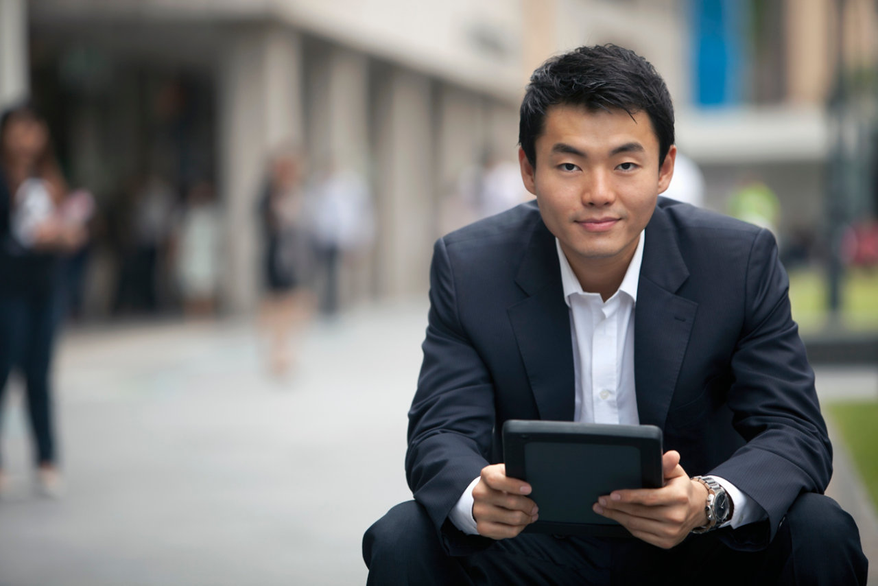 smiling man outside crouched down using tablet
