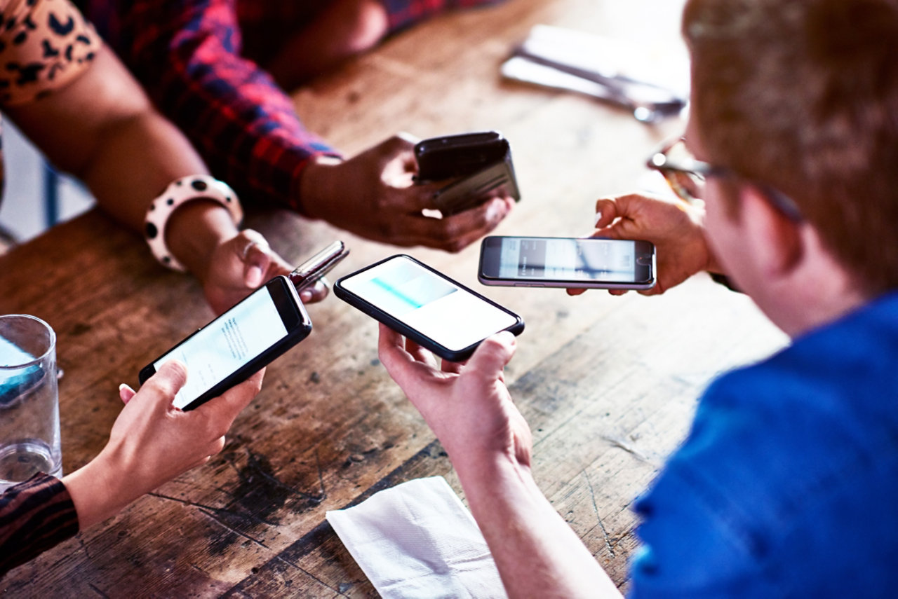 multiple hands holding phones at coffee table