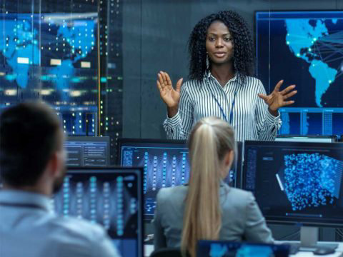 analyst talking to colleagues in front of screens with data