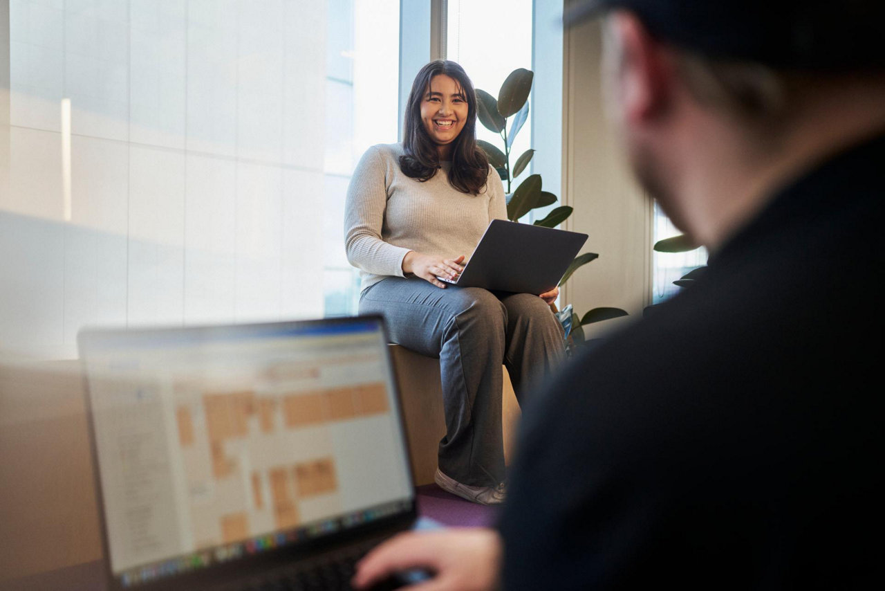 person in office casually sitting on a windowsill with laptop