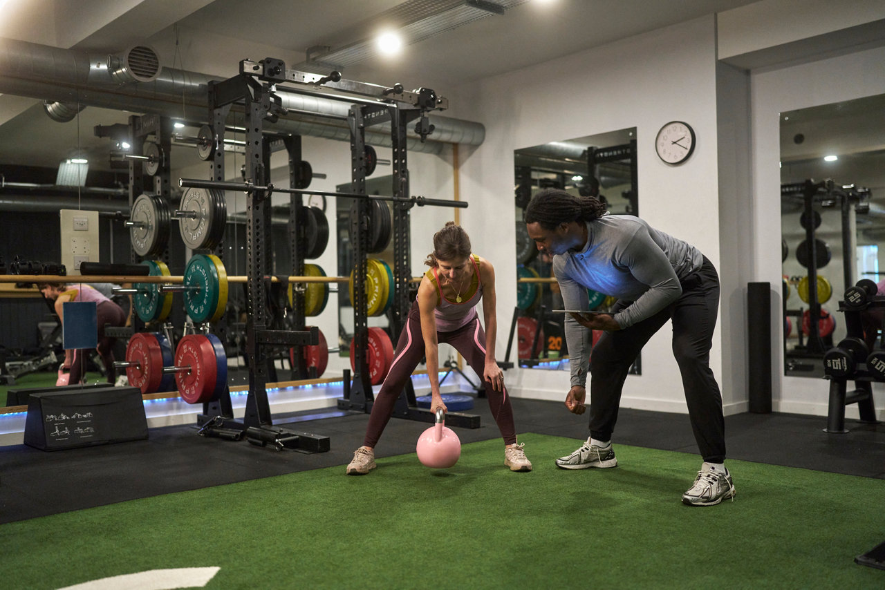 personal trainer with tablet assists another person at the gym