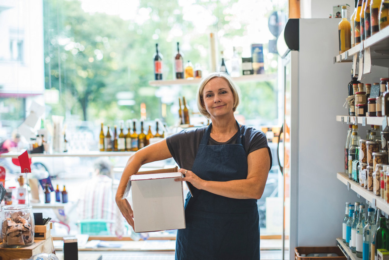 portrait of confident female owner carrying cardboard box in deli