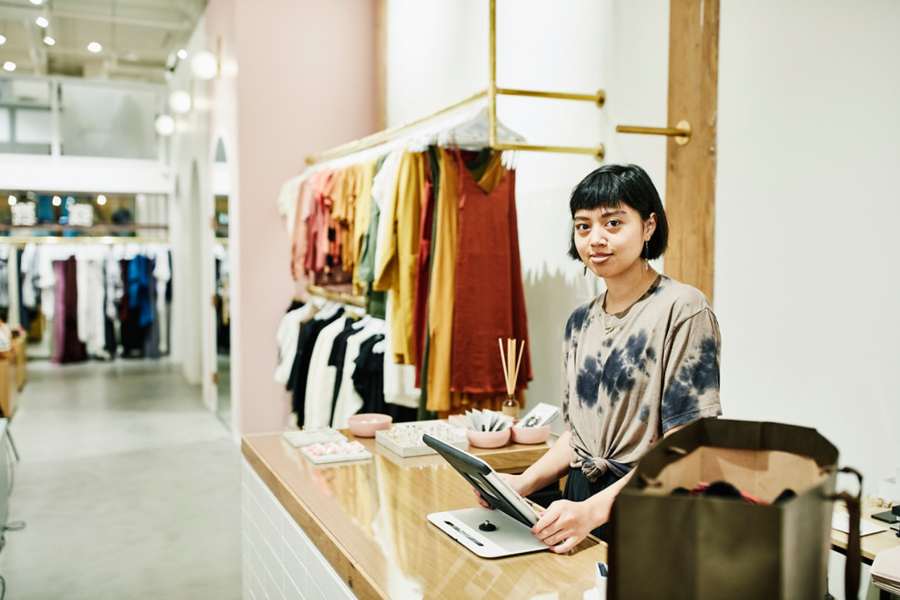 portrait of shop owner standing behind register in clothing boutique