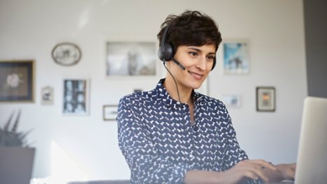 Smiling woman at home with headset using laptop