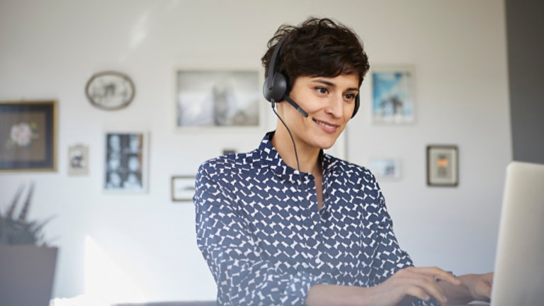 Smiling woman at home with headset using laptop