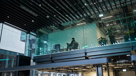 person in modern glass office working on laptop