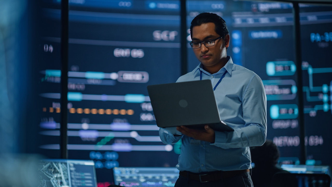 man using laptop infront of large screen with digital display